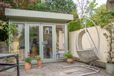 Salthouse Studio Home Office Contemporary grey garden office with glazed double doors, set on a patio with potted flowers and a hanging chair.